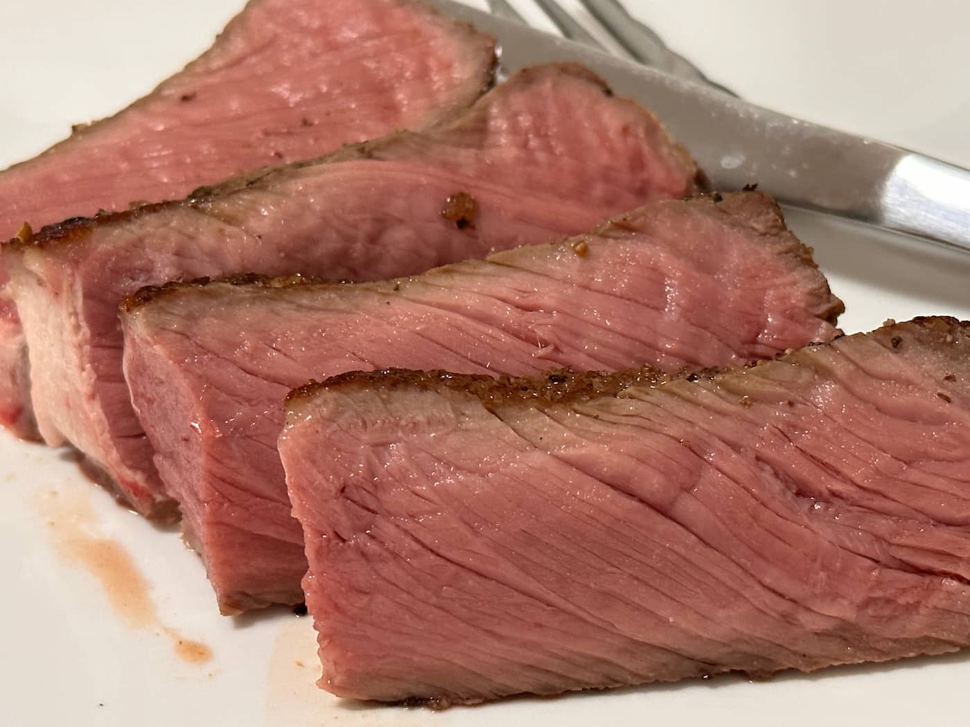 Steak cut into slices, served on a plate and ready to be eaten.