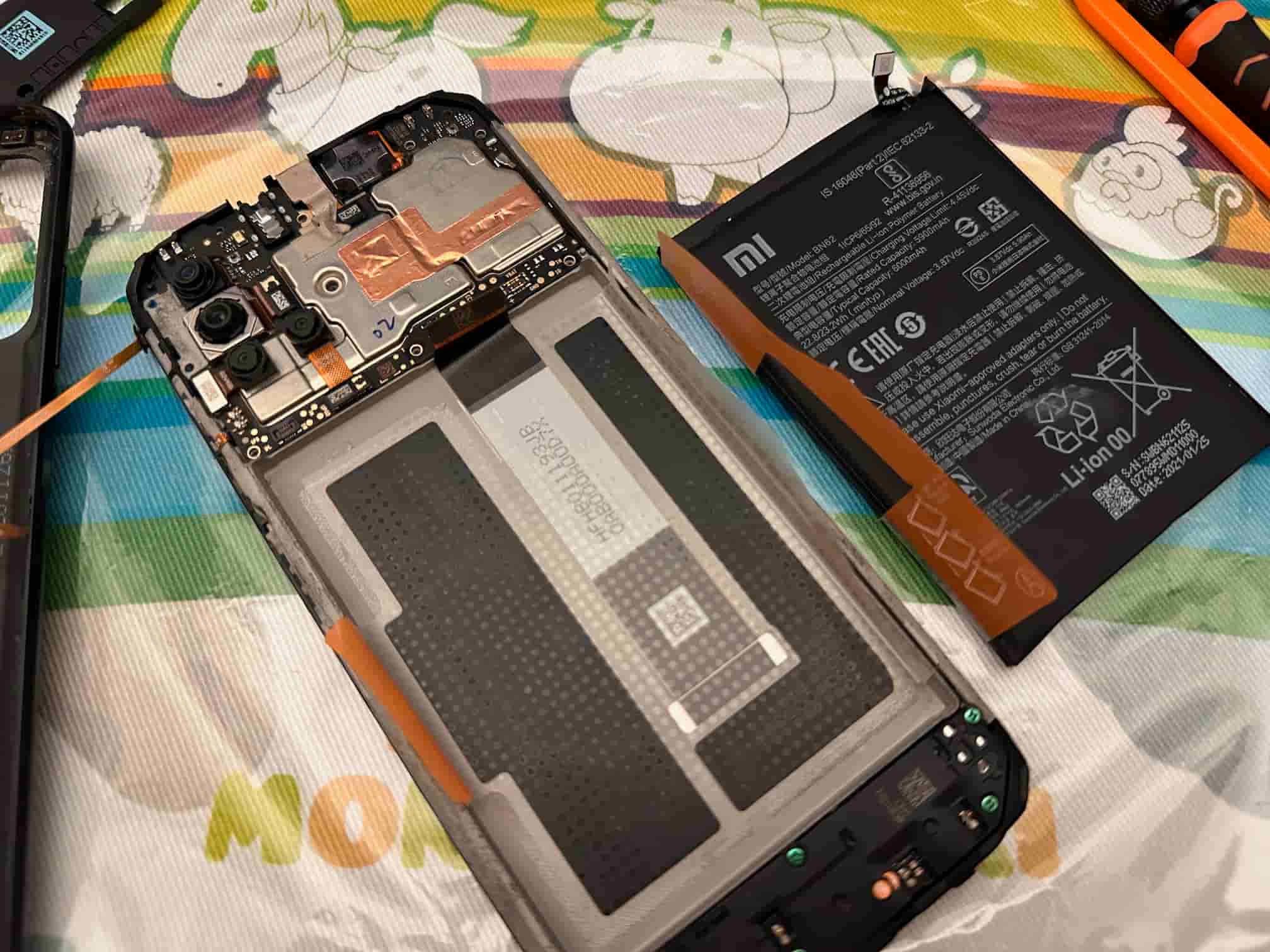 Disassembled Xiaomi Red 9T smartphone on a Bokujou Monogatari cloth with its battery removed