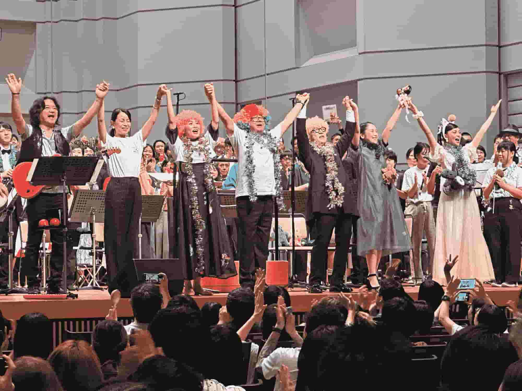 The BRA★BRA FINAL FANTASY 2024 concert cast stands on stage, holding hands and celebrating as the audience cheers